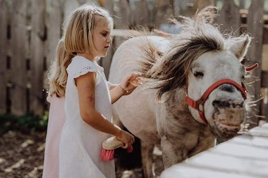 Mädchen pflegt ein Pony im Tierbereich des Familienhotel Mia Alpina in Tirol.