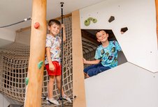 Ein Junge steht auf einem Balancierseil an einem Kletterbaum, ein anderer sitzt in einem Spielversteck mit Klettergriffen.