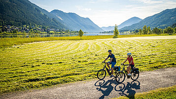 Ein Ausflug in Kaernten. Radfahrer fahren die Seenschleife und im Hintergrund erstrecken sich die Berge.