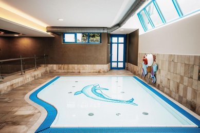Ein Innenpool mit flachem Becken, blauer Rutsche und Sitzbereich im Wellness- & Familienhotel Egger im Salzburger Land.