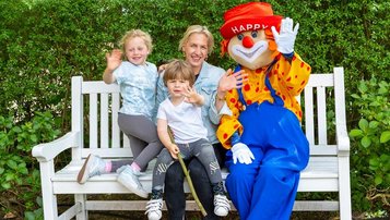 Kinder mit Maskottchen Happy auf der Parkbank im Garten des Familienhotels Gut Landegge im Emsland.