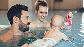 Eltern schwimmen mit ihrem Baby im Familienhotel Post Family Resort im Salzburger Land.