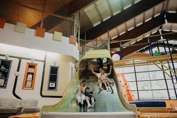 Kinder rutschen im Indoor-Spielbereich in einer Halle des Hotel Sonngastein im Salzburger Land eine breite Rutsche hinunter.