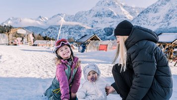 Zwei Kinder und ihre Mutter genießen den Schnee vor traumhafter Bergkulisse beim Familienhotel Tirolerhof