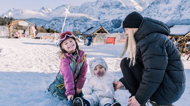 Zwei Kinder und ihre Mutter genießen den Schnee vor traumhafter Bergkulisse beim Familienhotel Tirolerhof