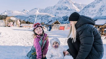 Zwei Kinder und ihre Mutter genießen den Schnee vor traumhafter Bergkulisse beim Familienhotel Tirolerhof