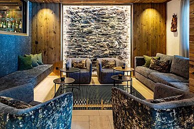 Gemütlich eingerichtete Lounge mit einer Steinwand und Sofas im Adler Familien- & Wohlfühlhotel in Tirol.