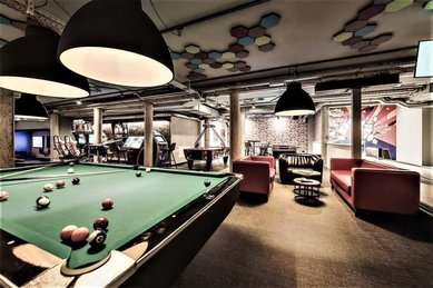 In der Playfactory des Familienhotel Mia Alpina in Tirol steht ein Billardtisch mit Sitzbereich, Lampen und bunter Einrichtung.