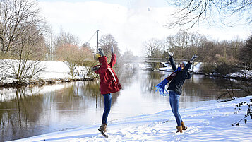 Zwei Frauen spielen mit dem Schnee am Dortmund-Ems-Kanal. Im Hintergrund ist eine Brücke zusehen.