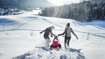 Eltern haben mit ihrem Kind viel Spaß beim Rodeln in Seefeld Tirol im Familienhotel Das Kaltschmid. 
