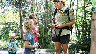 Drei Kinder beim Wandern auf einem Erlebnispfad im Schwarzwald gemeinsam mit einer Kinderbetreuerin.