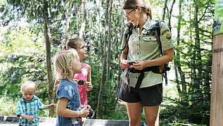 Drei Kinder beim Wandern auf einem Erlebnispfad im Schwarzwald gemeinsam mit einer Kinderbetreuerin.