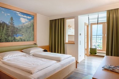 Helles Familienzimmer mit gemütlichem Bett und Bergblick im Familienhotel Amiamo im Salzburger Land.