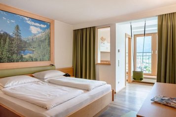 Helles Familienzimmer mit gemütlichem Bett und Bergblick im Familienhotel Amiamo im Salzburger Land.