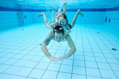 Vater und Tochter tauchen gemeinsam im Pool des Familienhotels Das Bayrischzell