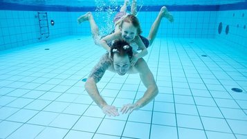 Vater und Tochter tauchen gemeinsam im Pool des Familienhotels Das Bayrischzell