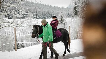 Glückliches Mädchen reitet auf einem Pferd im Reitunterricht im Familienurlaub in der Steiermark. 