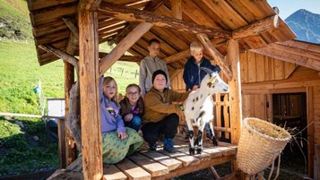 Kinder sitzen gemeinsam mit einer Ziege im Ziegenhäuschen vom Freilaufgehege im Familienhotel Oberkarteis im Salzburger Land.