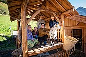 Kinder sitzen gemeinsam mit einer Ziege im Ziegenhäuschen vom Freilaufgehege im Familienhotel Oberkarteis im Salzburger Land.