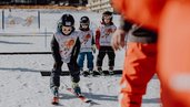 Beim Skikurs des Familienhotel Mia Alpina in Tirol fahren Kinder mit Skihelmen und Skibrillen durch den Schnee.