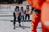 Beim Skikurs des Familienhotel Mia Alpina in Tirol fahren Kinder mit Skihelmen und Skibrillen durch den Schnee.
