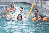 Eine Familie genießt gemeinsam mit Schwimmhilfen und Wasserspielzeug die Zeit im lebhaften Innenpool des Hotels Feldberger Hof.