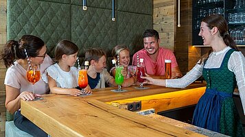 Eltern sitzen mit ihren Kindern an der Bar und lassen sich einen Cocktail servieren im Adler Familien- & Wohlfühlhotel in Tirol.