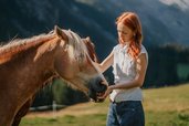 Eine Frau steht auf einer Wiese neben einem Pferd vor der Berglandschaft des Hotels Bella Vista in Südtirol.