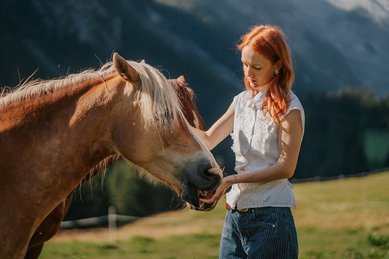 Eine Frau steht auf einer Wiese neben einem Pferd vor der Berglandschaft des Hotels Bella Vista in Südtirol.