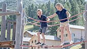 Ein Mädchen sitzt auf einem Klettergerüst auf dem Outdoor-Spielplatz des Familienhotels Gorfion in Liechtenstein.