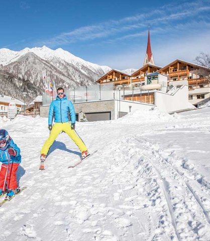 Vater und Kind fahren auf der Piste direkt vor dem Familienhotel Huber in Südtirol Ski