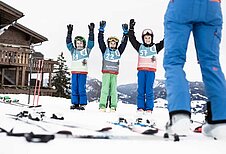 Drei Jungs stehen im Schnee und halten beim Skikurs vom Allgäuer Berghof die Hände in die Höhe.