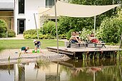 Eltern entspannen am Sonnendeck während die Kinder im Sandkasten des Familien Wellness Hotels Seeklause spielen.