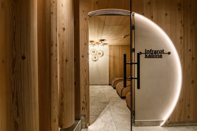 Stimmungsvoll beleuchtete Infrarotkabine im Zauchenseehof mit organisch geformten Liegen, Holzverkleidung und rundem LED-Lichtbogen an der Eingangstür.