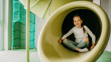 Fröhliches Mädchen am Ende einer Indoor-Rutsche im Familienhotel Friedrichshof.
