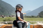 Mädchen reitet lächelnd auf einem Haflinger vor Bergkulisse im Familienhotel Kindl.