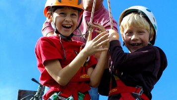 Zwei Jungs hängen mit Kletterausrüstung an einer Seilrutsche und freuen sich auf das Abenteuer.