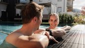 Zwei Erwachsene entspannen sich am Beckenrand des Außenpools des Familienhotels Scherer.