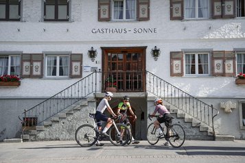 Drei Radfahrer machen eine Pause vor dem Eingang des Familienhotel Sonne Bezau.