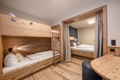 Familienzimmer im Familienhotel Zauchenseehof mit gemütlichem Kinderstockbett aus Holz und separatem Elternschlafbereich mit Vorhang für wohltuende Privatsphäre.
