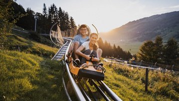 Ein Mann und eine Frau sitzen im Rodel der Ganzjahresrodelbahn Alpsee Coaster in Immenstadt im Allgäu.