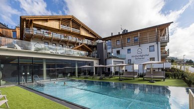 Außenansicht des Familienhotels Almfamilyhotel Scherer mit beheiztem Pool und Liegebereich in sonniger Lage in Osttirol.