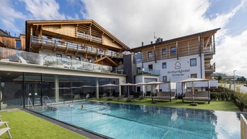 Außenansicht des Familienhotels Almfamilyhotel Scherer mit beheiztem Pool und Liegebereich in sonniger Lage in Osttirol.