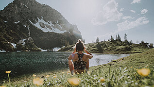 Eine Frau sitzt am See und genießt den Sommer im Allgäu. Der Tag ist schön und im Hintergrund steht ein Berg.