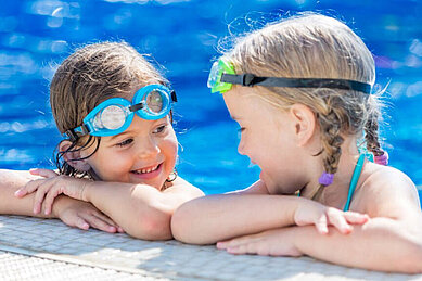 Zwei Mädchen am Beckenrand im Pool des Familienhotels Kaltschmid in Tirol.