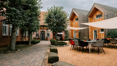 Gemütlicher Innenhof des Familienhotels Landhaus Averbeck mit modernen Holzhäusern, Sitzgelegenheiten und schattenspendenden Sonnensegeln.