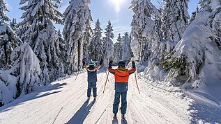 Zwei Kinder beim Skifahren im Familienurlaub in Deutschland im Winter.