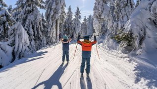 Zwei Kinder beim Skifahren im Familienurlaub in Deutschland im Winter.