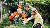 Familie mit zwei Kindern streichelt ein Meerschweinchen im Garten des Kinderhotels Sailer in Tirol.