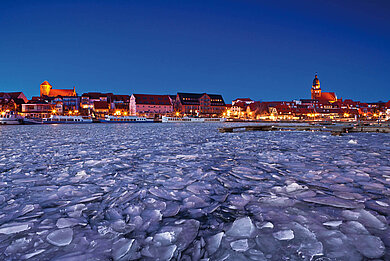 Ein See ist eingefroren mit blick auf eine Stadt im Abendlicht.